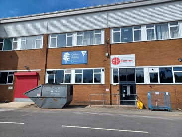 The GIS health care building which is a brick building with a red GIS health care sign on it and there is a grey skip outside.