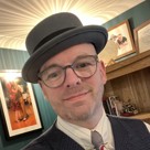 Paul smiling and dressed smartly with a hat and suit.